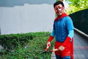 Superhero team demonstrating their dedication to beautifying the surroundings in Thailand, skillfully trimming a hedge during a team-building event.
