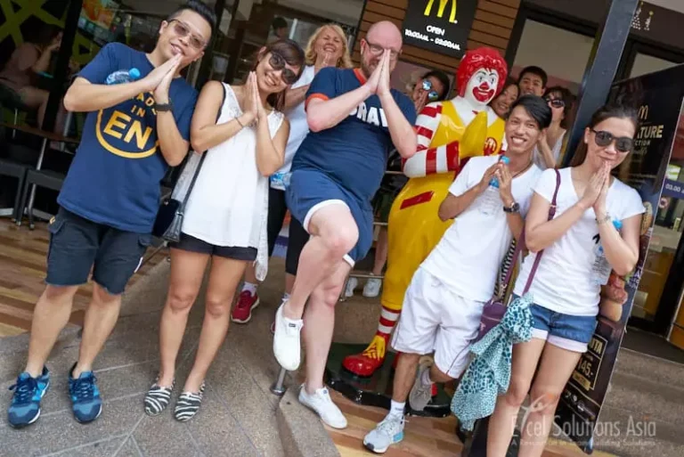 Happy team members striking a pose next to a famous clown statue during a scavenger hunt in Pattaya, Thailand.
