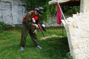 A player crouching low behind a barricade, eyes keenly scanning the battlefield, ready to take a shot while minimising exposure, in paintball combat.