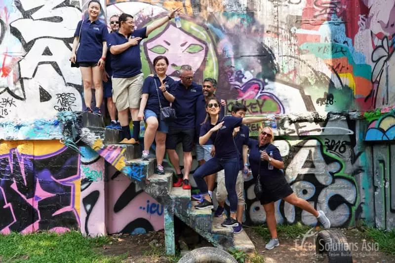 A group striking a pose amidst the colourful and artistic graffiti of Bangkok's vibrant graffiti park, during their journey in the Amazing Race.