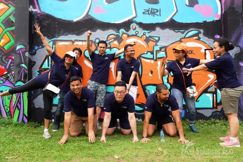 A group surrounded by the captivating murals and street art of Bangkok's graffiti park, as they take a group photo during their Amazing Race.